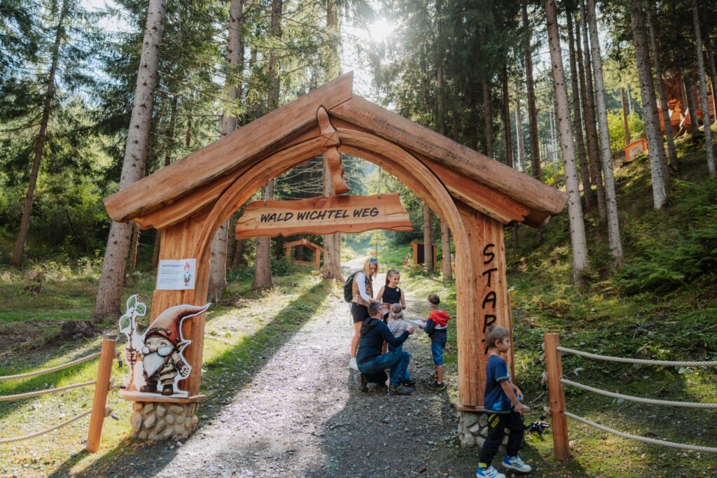 Der Wichtelpark ist ein tolles Ausflugsziel am Drauradweg. Eine Familie mit Kindern spaziert am Sillianer Waldweg um Willi dem Wichtel zu helfen.