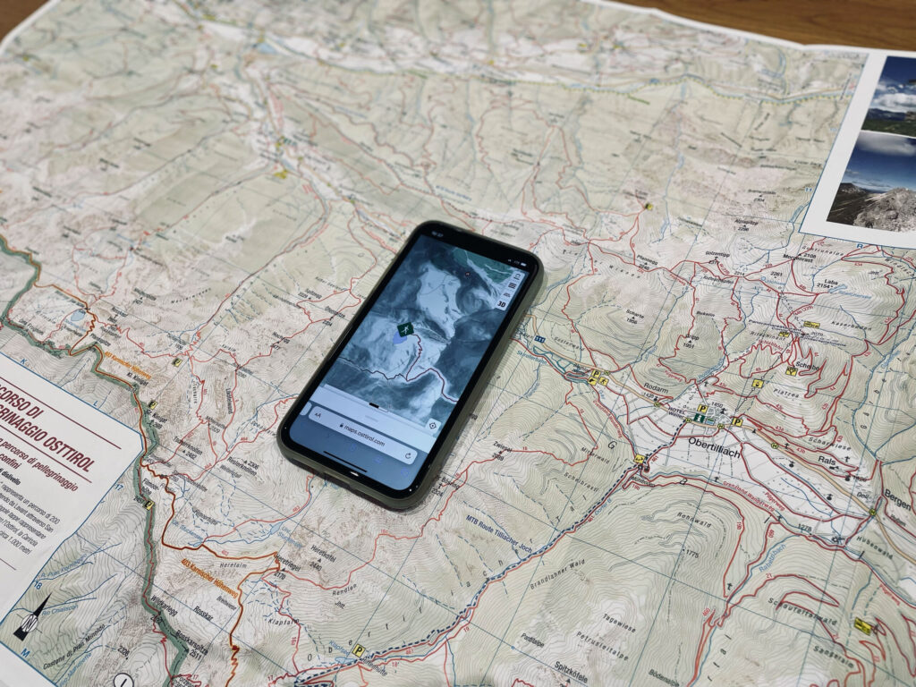 Ein Smartphone liegt auf einer physischen Landkarte. Eine gute Tourenplanung ist wichtig, um einem alpinen Notfall bestmöglich vorzubeugen.