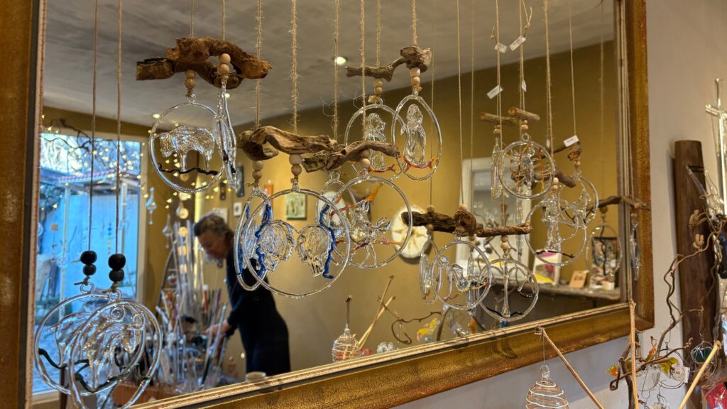 Glaskunstwerke von Veronika Petutschnig, kunstvoll arrangiert mit Holz. Im Spiegelbild ist die Künstlerin in ihrer Werkstatt zu sehen.