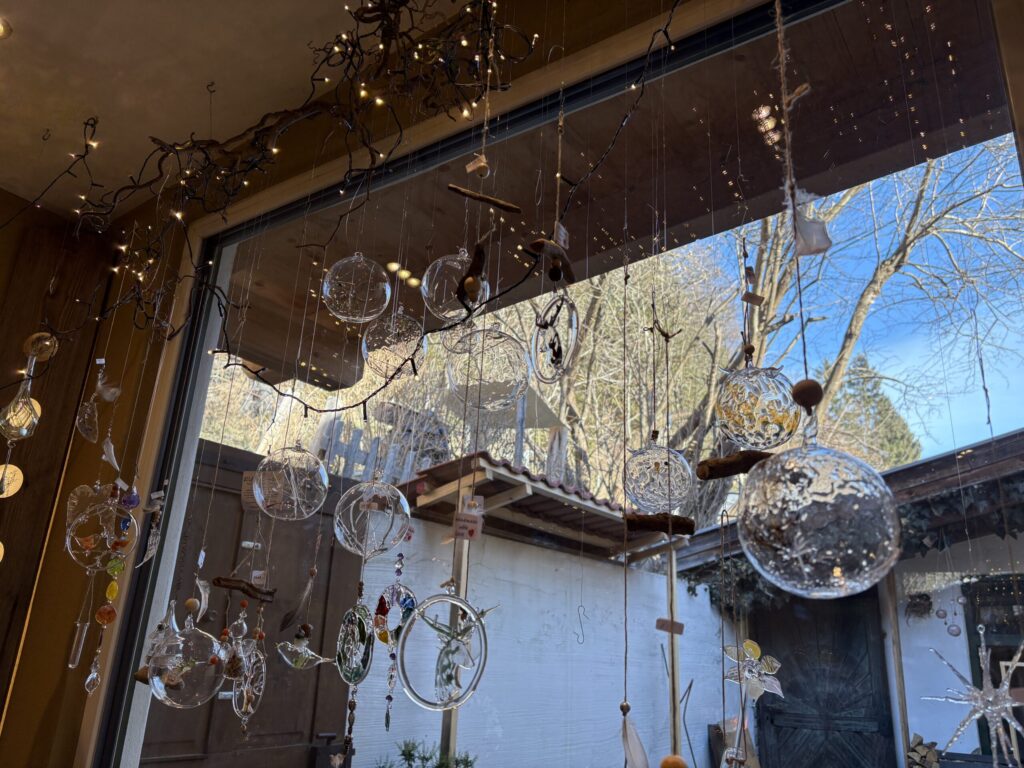 Glaskugeln und Ornamente hängen in der Glasgrün-Werkstatt am Fenster, verziert mit Zweigen und einer Lichterkette.