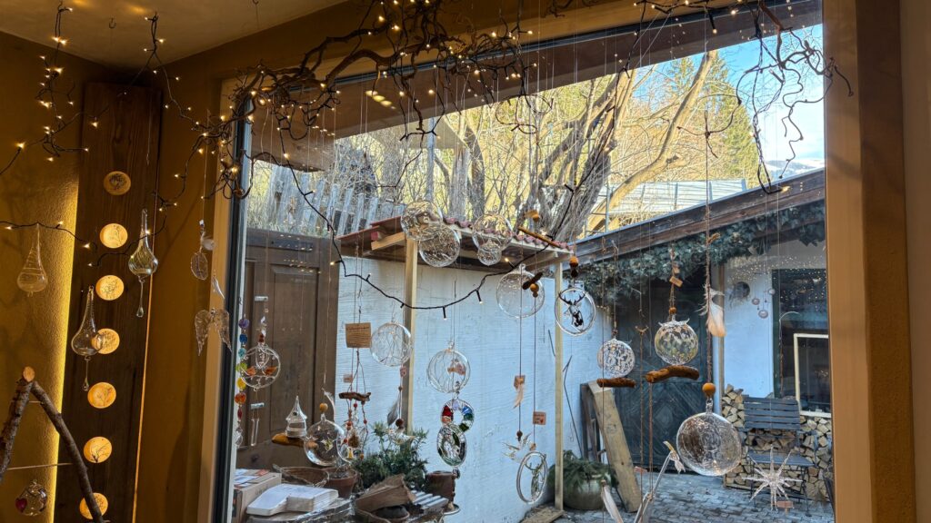 Glaskugeln und Ornamente hängen in der Glasgrün-Werkstatt am Fenster, verziert mit Zweigen und einer Lichterkette.