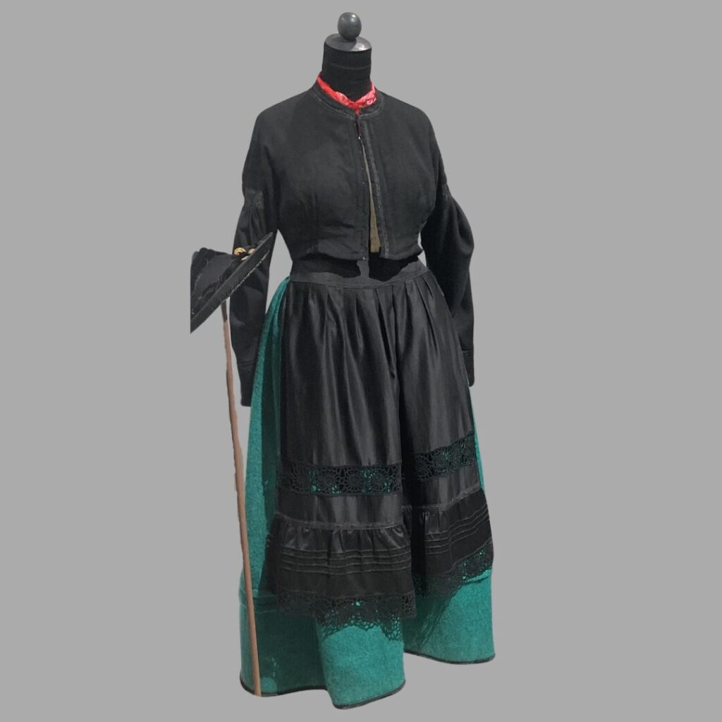 Man sieht die Lienzer Tracht vor einem grauen Hintergrund. Die Tracht ist ein Beispiel für frühe synthetische Färbetechniken, die bereits um 1835/1840 in Gebrauch waren.