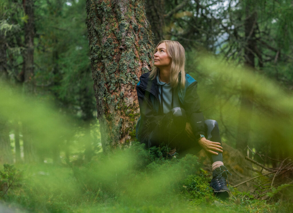 Eine Frau sitzt an einen Baum gelehnt im Wald Osttirols.