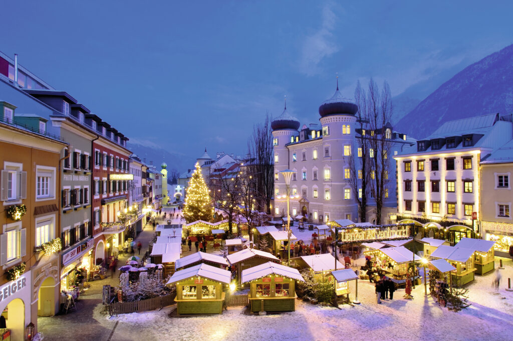 Ansicht des Adventmarkts in Lienz von oben. Die Hütten sind mit Lichterketten geschmückt und im Hintergrund sieht man den Adventkalender der Liebburg. Die Dächer sind mit Schnee bedeckt.