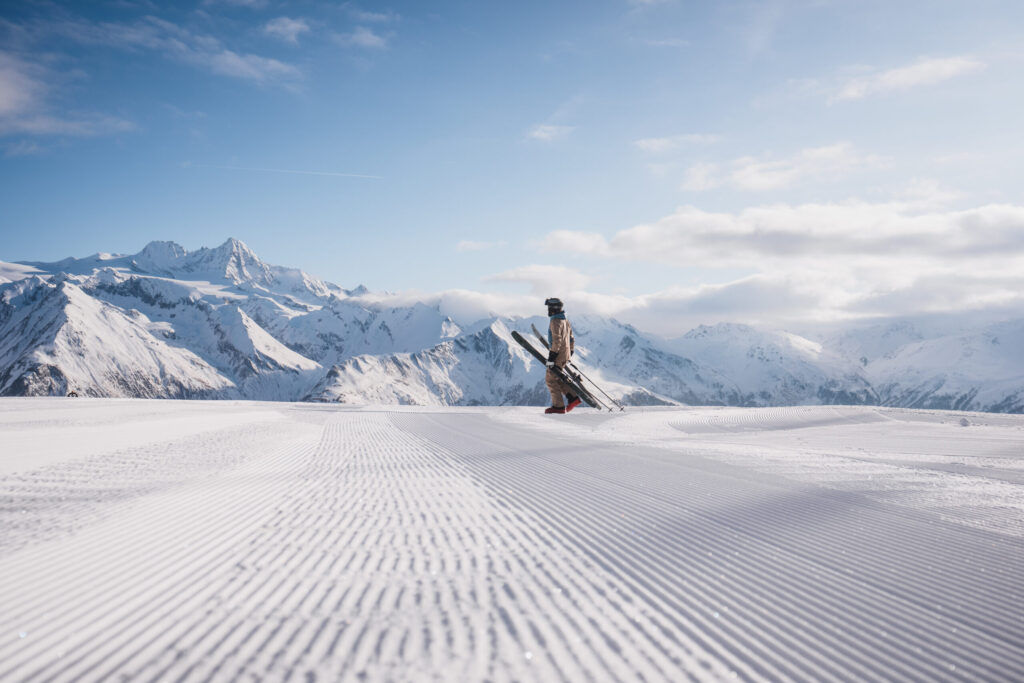 Eine Person im Skianzug und mit Skiern in der Hand befindet sich auf der frisch präparierten Piste im Angesicht der Hohen Tauern und es Großglockners.