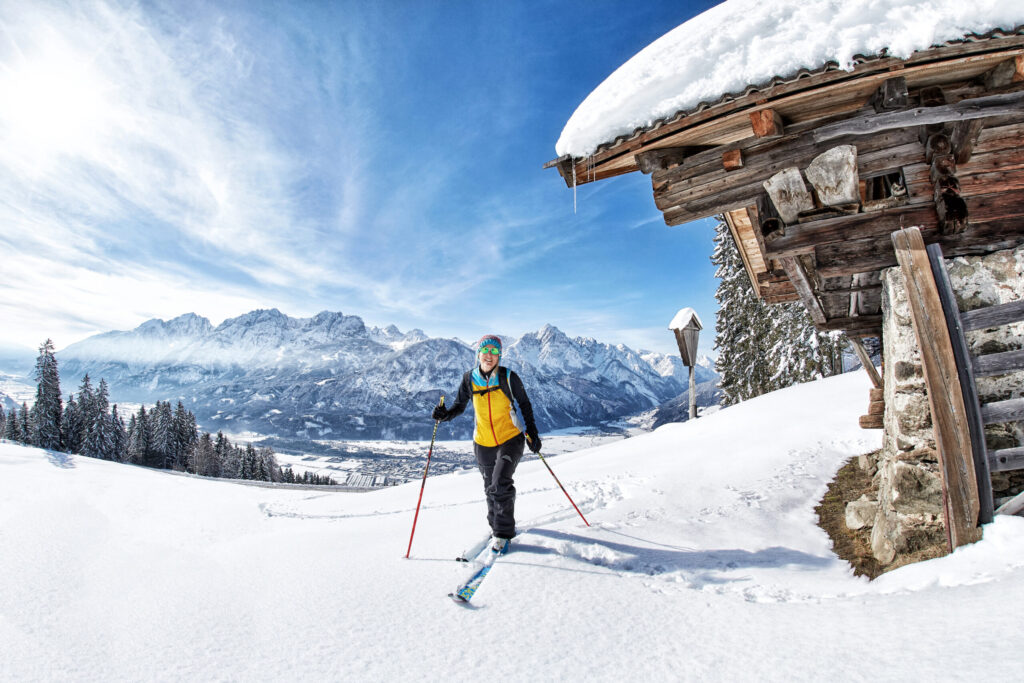Eine Wintersportlerin in schwarz-gelber Winterkleidung auf einer Skitour am Lienzer Zettersfeld in Osttirol, im Hintergrund die Stadt und die Lienzer Dolomiten.