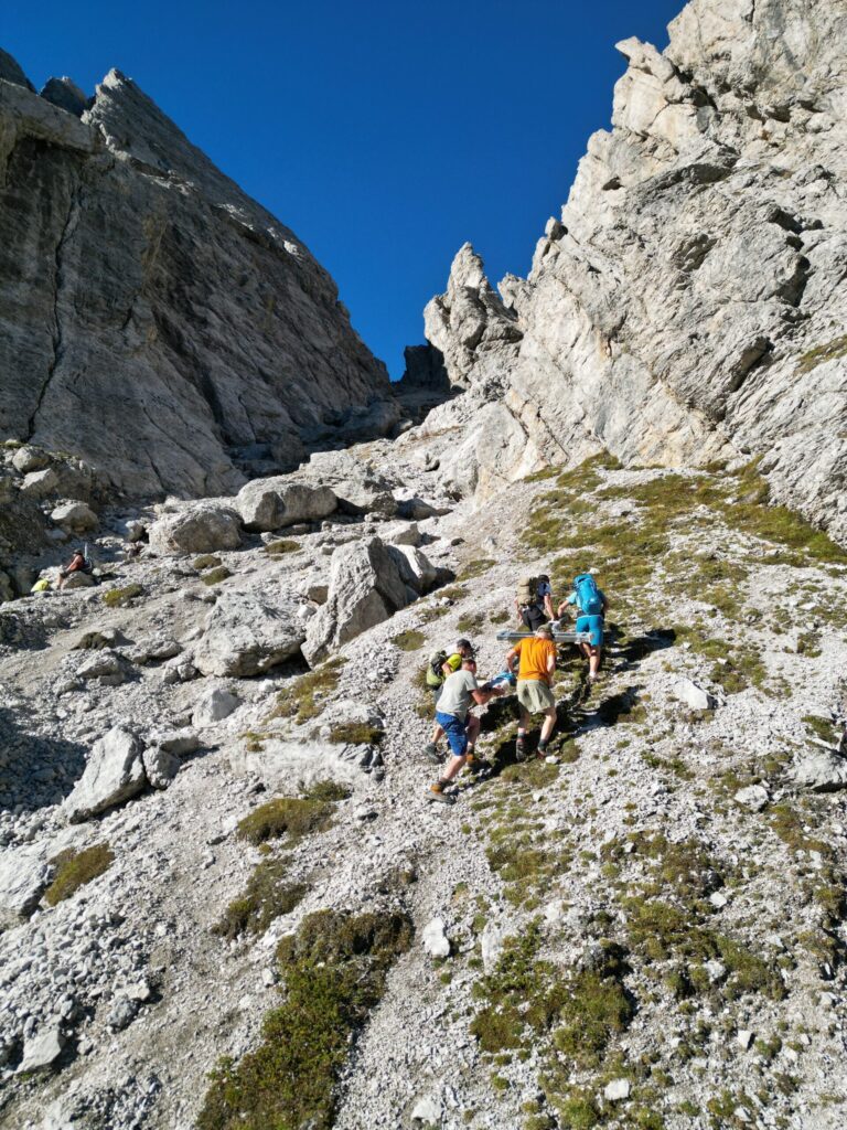 Mehrere Personen tragen das schwere Metallkreuz Richtung Gipfel der Gamswiesenspitze.