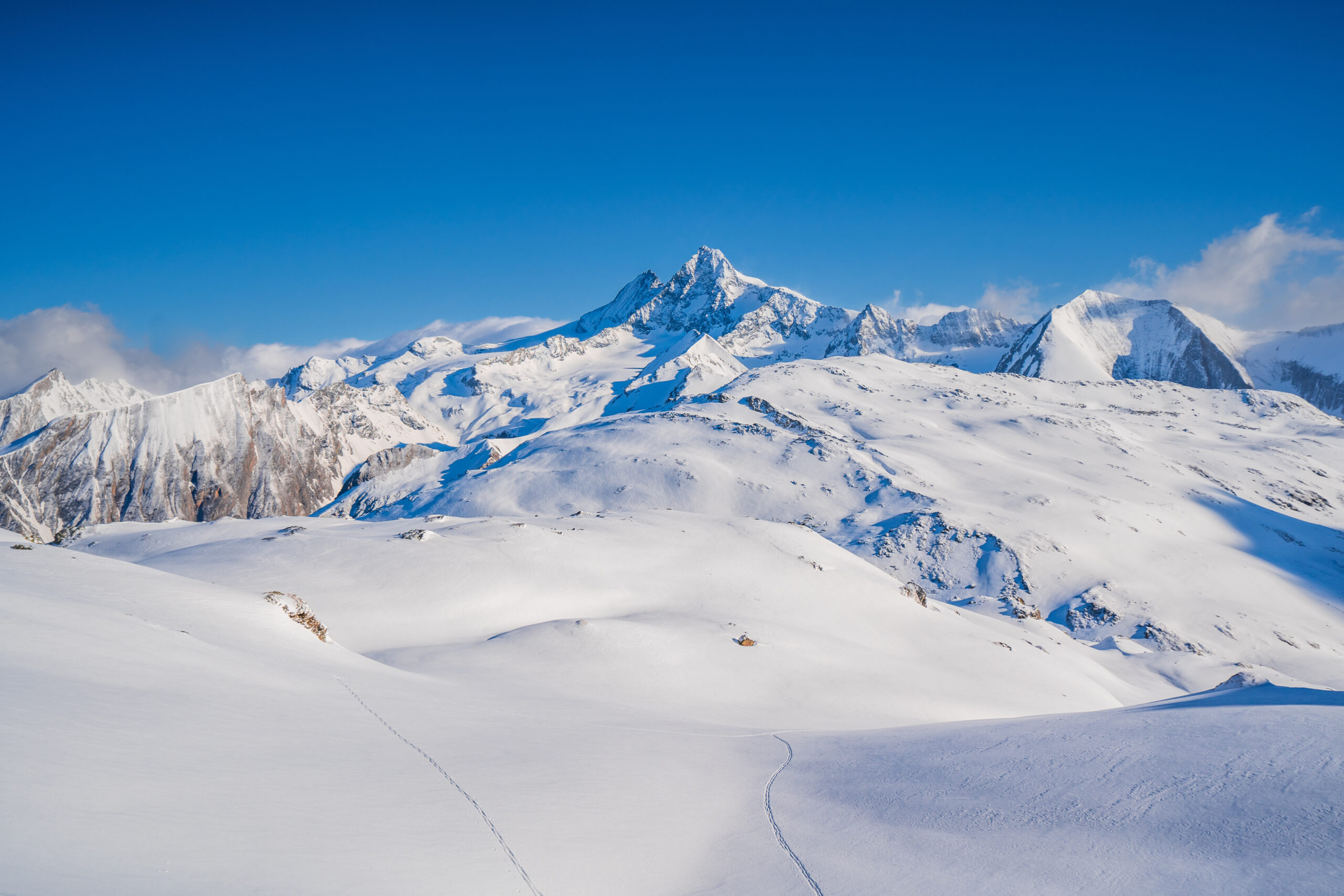Weite, schneebedeckte Berglandschaft beim Bösen Weibele in Osttirol mit Skitourenspuren im Vordergrund und dem Großglockner unter blauem Winterhimmel.