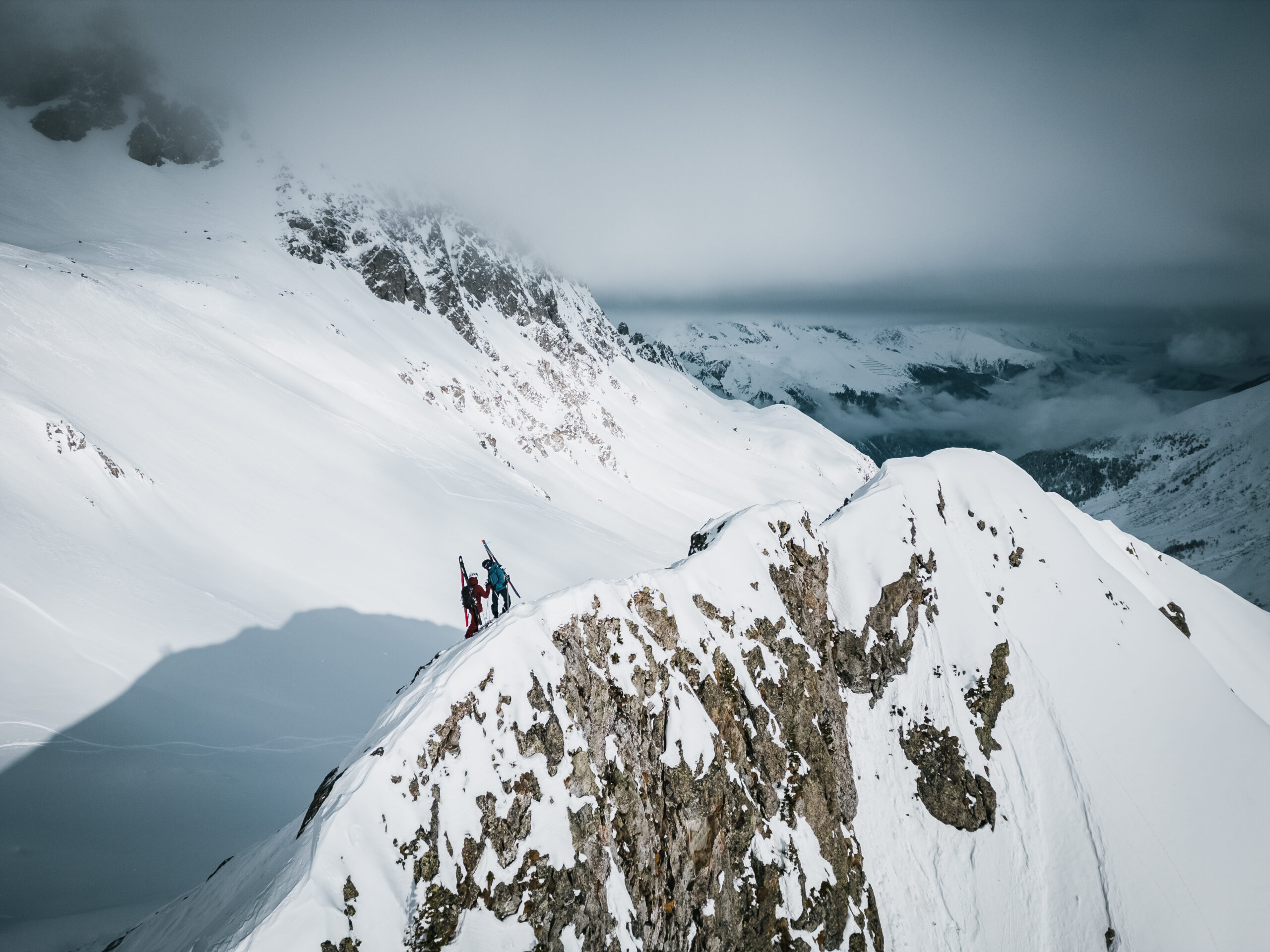 Zwei Skitourengeher mit Ski am Rucksack steigen über einen schneebedeckten Grat an der Roten Wand im Defereggental in Osttirol auf.
