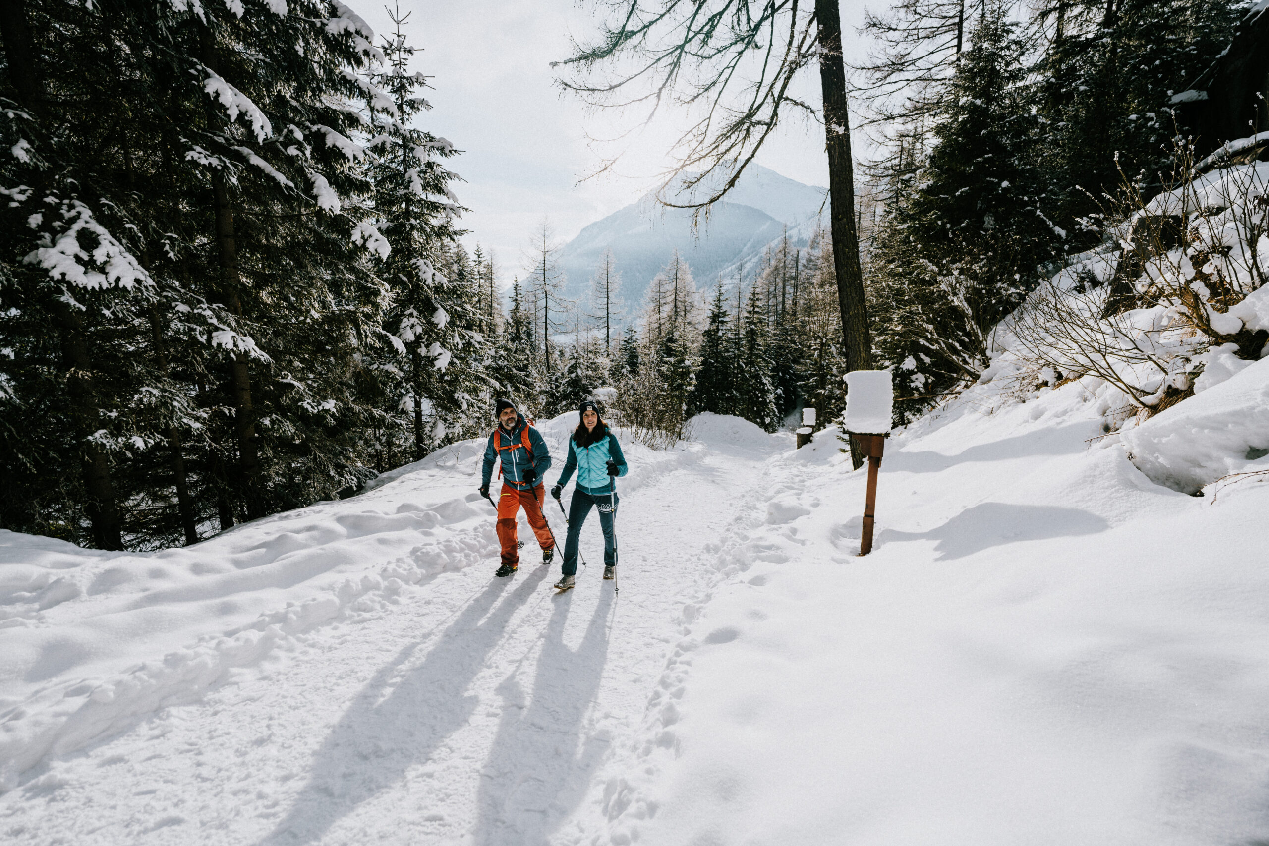 Zwei Personen beim Winterwandern auf einem verschneiten Waldweg in Kals am Großglockner in Osttirol